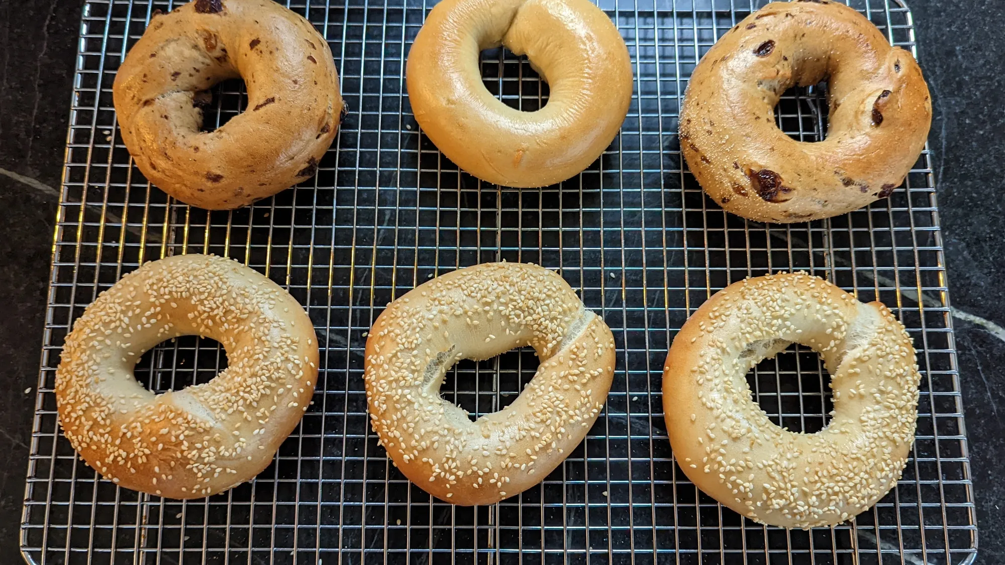 Finished cinnamon-raisin, plain and sesame bagels on a cooling rack.